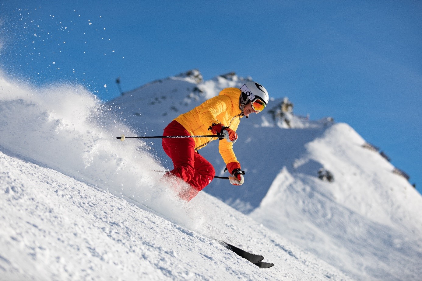 Un skieur en tenue rouge et jaune dévale une piste en laissant une trainée de neige