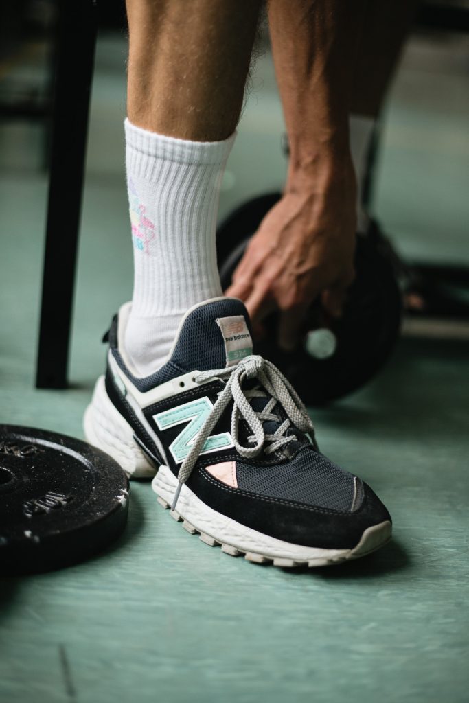 Photo de la demie jambe d'un homme chaussé avec une basket de sport, une chaussette haute et des poids avant une séance de préparation physique