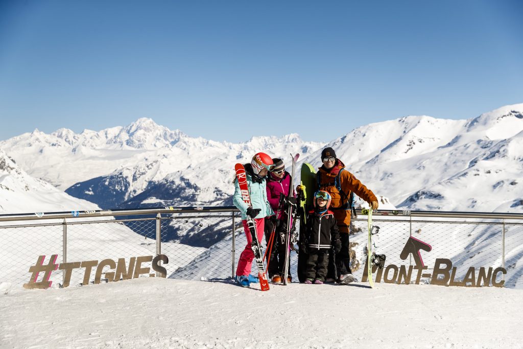 Une famille prise en photo devant une chaine de montagne en haut de la station Tignes.
